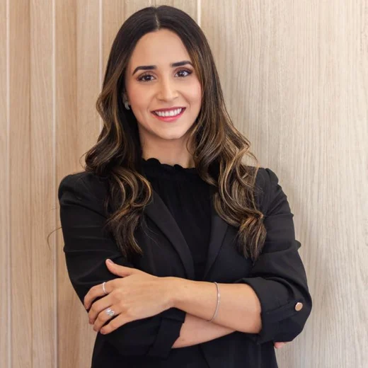 Vanessa Takuno, nutricionista, sorrindo, de blazer preto e braços cruzados.